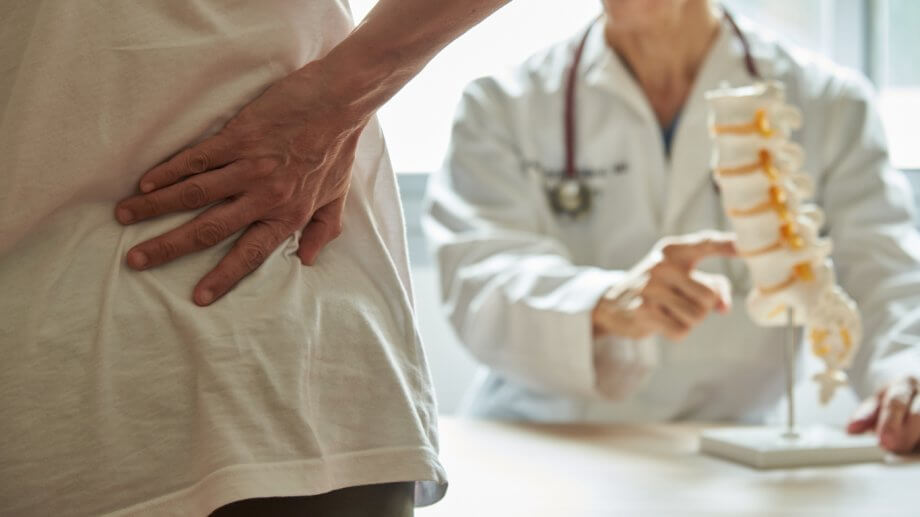 Photograph of a person holding their lower back in pain as a doctor talks to them in an office setting.